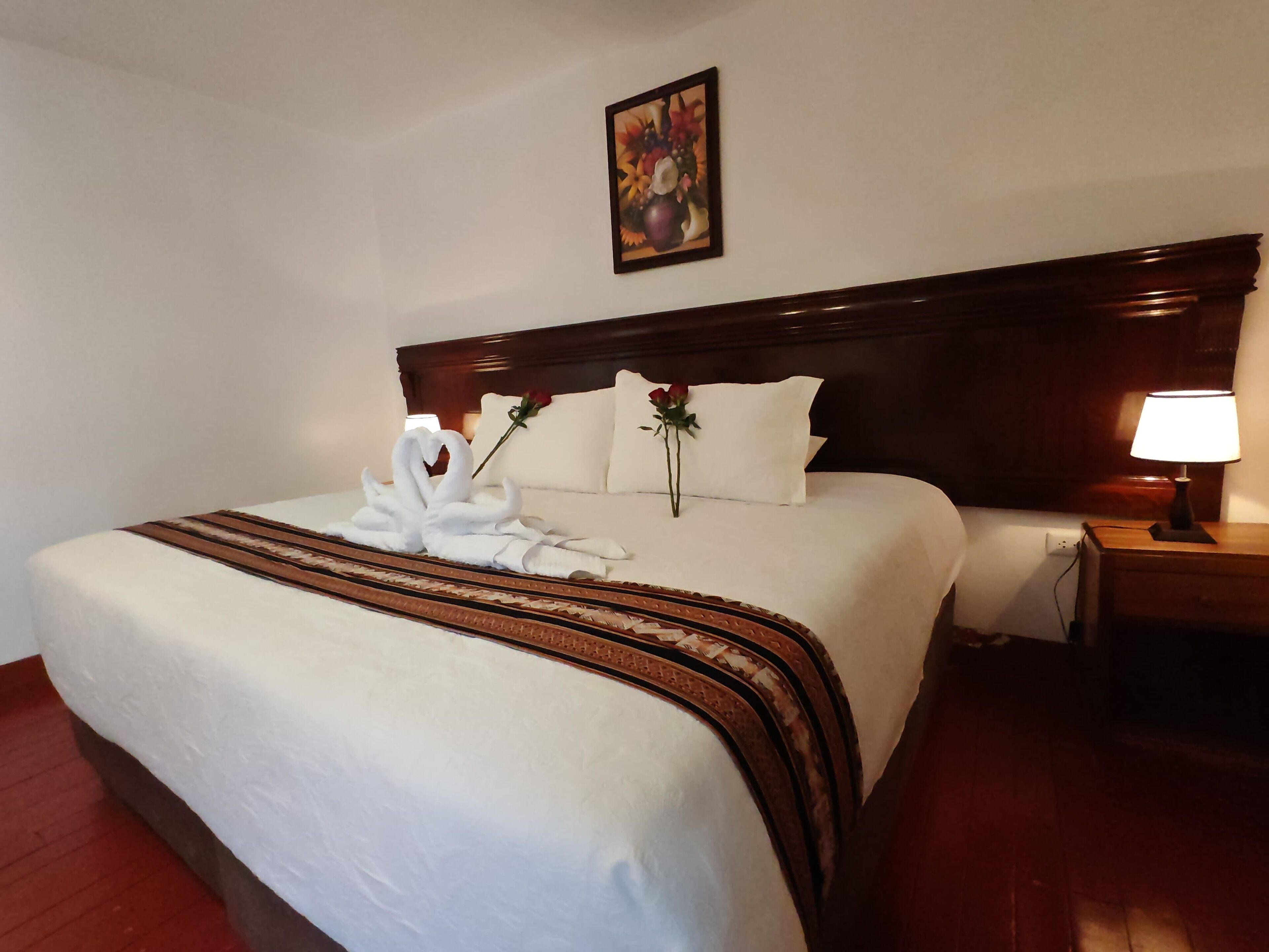 A neatly made bed with white linens, a decorative towel arrangement, and a single rose on the pillows.