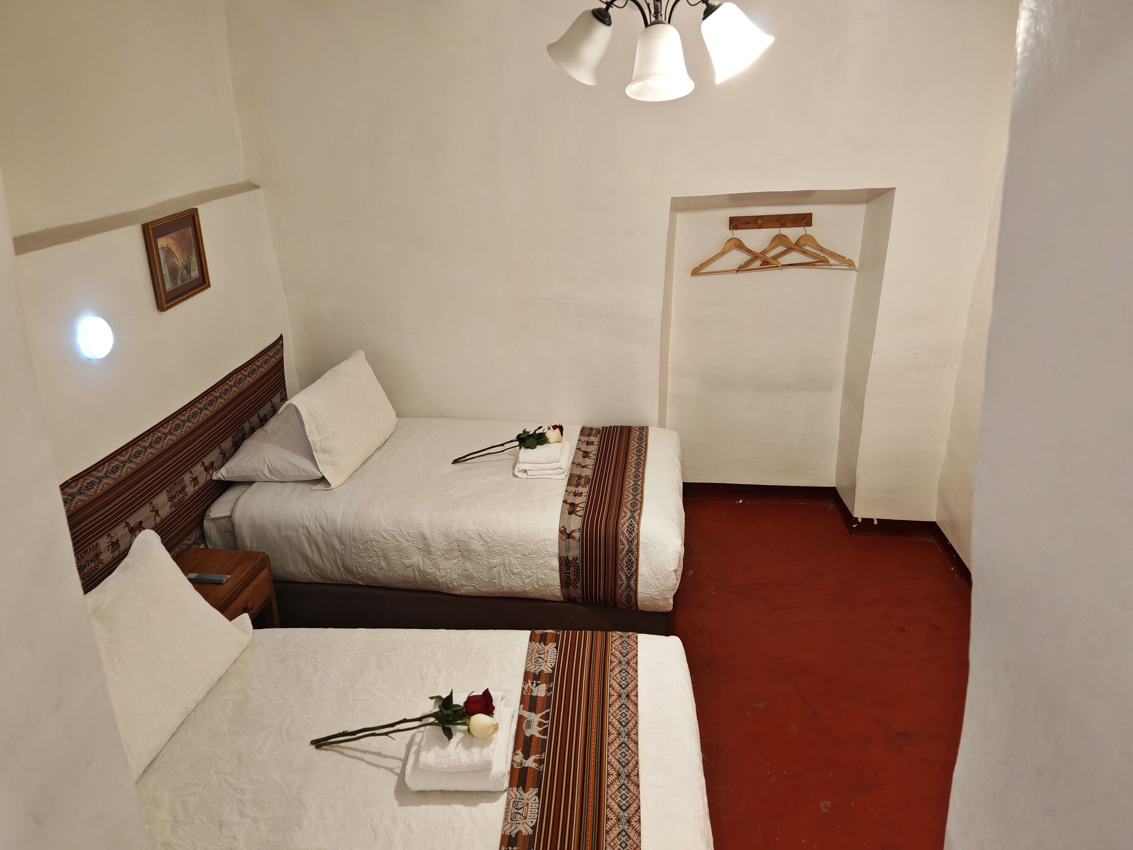 A hotel room with two beds, a wooden headboard, a red carpet, and a hanging clothes rack.