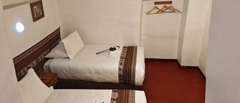 A hotel room with two beds, a wooden headboard, a red carpet, and a hanging clothes rack.