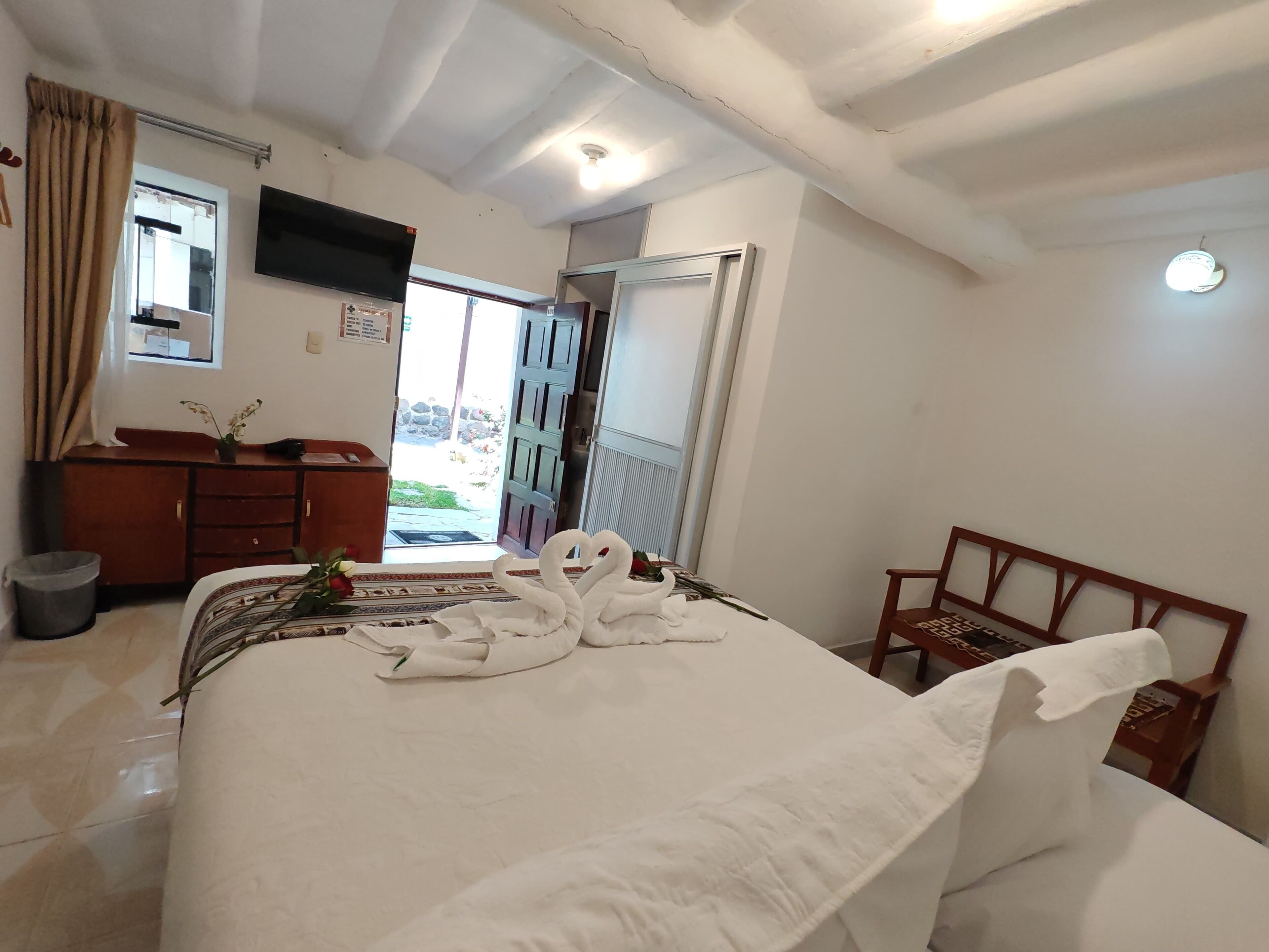 A hotel room with a bed, a wooden dresser, a TV, and a balcony with a view.