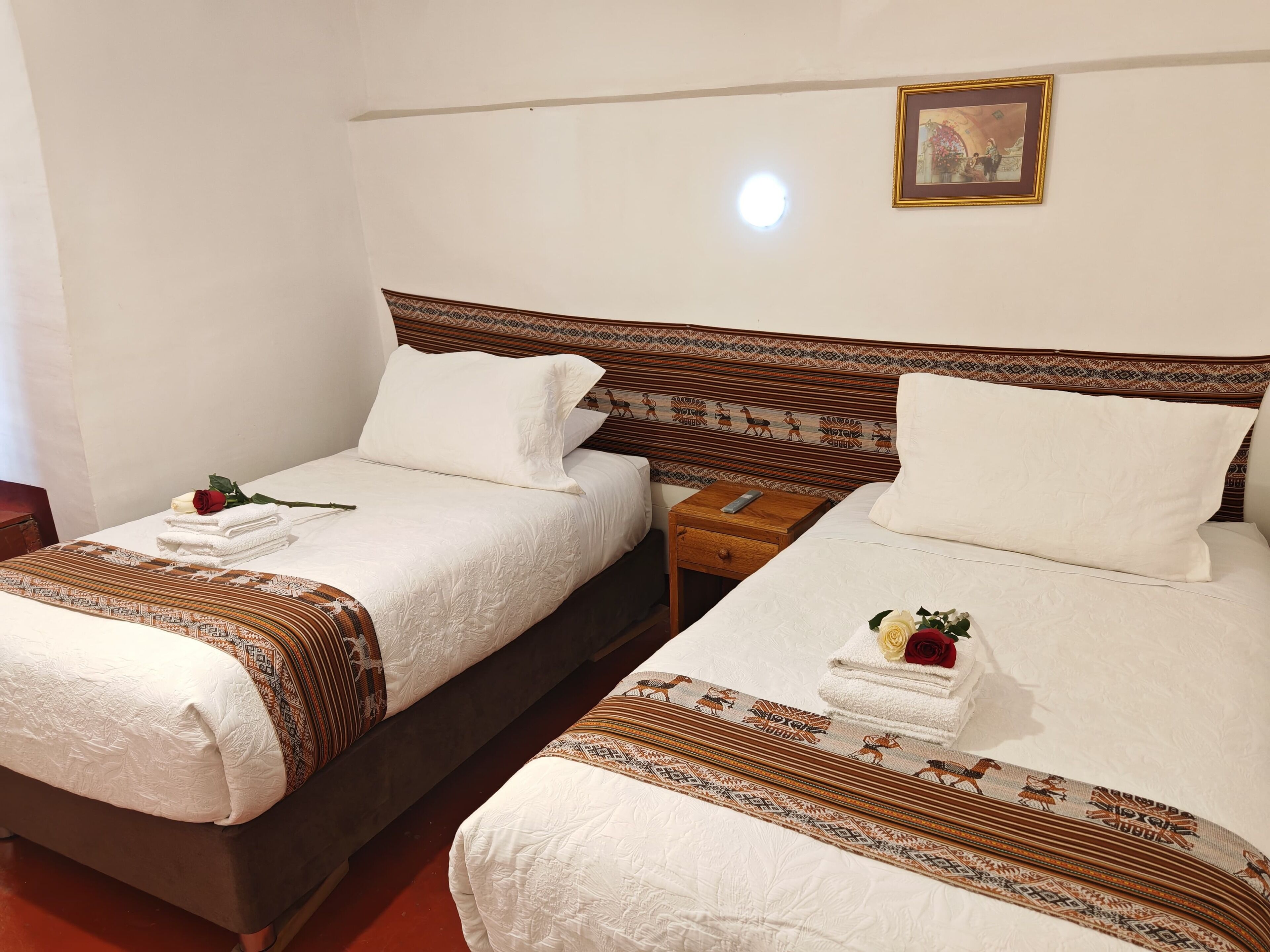 Ein Hotelzimmer mit zwei Betten, jeweils mit gemusterten Bettdecken und Kissen, einem Nachttisch mit Fernbedienung und einem gerahmten Bild an der Wand.