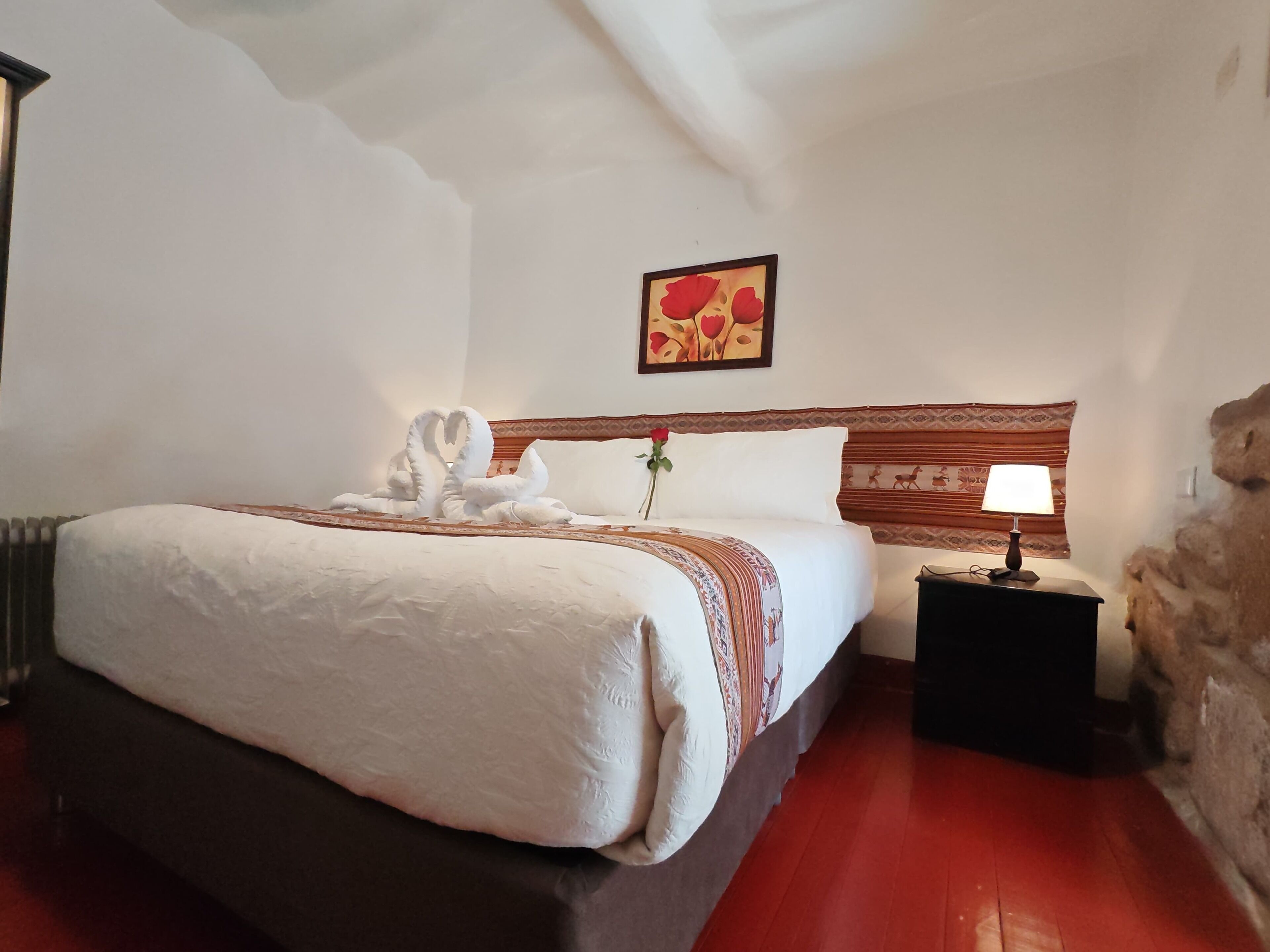 Ein Hotelzimmer mit einem großen Bett, einem Nachttisch mit Lampe, einem Wandbild und einer Steinwand.