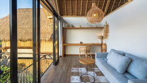 A modern interior with a thatched roof, a sofa, a table, and a hanging light fixture. - Green Harmony Villa by Betterplace (Ubud)