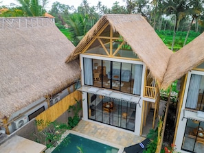 A two-story house with a thatched roof, a balcony with a glass enclosure, and a swimming pool.