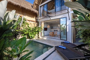 A modern house with a swimming pool, outdoor dining area, and lush tropical plants.