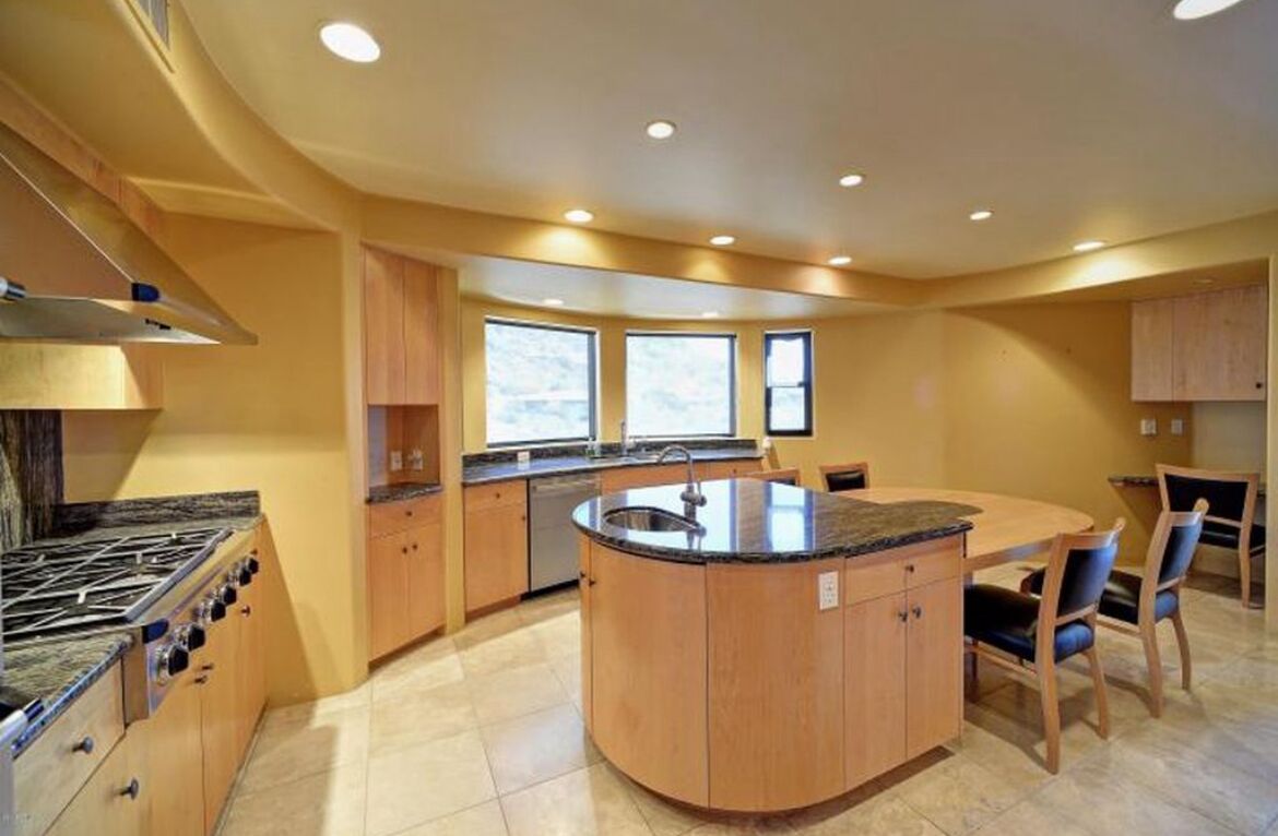 A modern kitchen with a central island, built-in oven, and ample natural light from large windows.