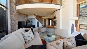 A spacious living area with a curved staircase, a fireplace, and a large window offering a view of the outdoors.
