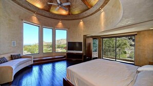 A bedroom with a large bed, a TV, and a seating area with a view of the outdoors.