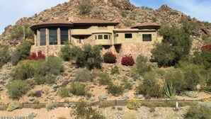 A two-story house with a curved roof, situated on a rocky hillside with sparse vegetation.