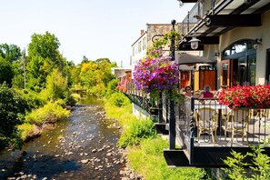 Ein Flussufer-Café mit Außenbestuhlung, einer Steinbrücke und üppiger Vegetation.