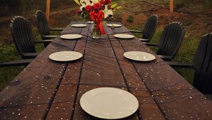 Un espacio de comedor al aire libre con una mesa de madera preparada para seis personas, rodeada de sillas y luces colgantes.
