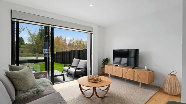 Un salon moderne comprenant un canapé, une table basse, un téléviseur posé sur un meuble en bois et une porte-fenêtre coulissante donnant sur un jardin.