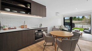Une cuisine moderne avec des meubles de couleur bois foncé, des carreaux de céramique blancs disposés en motif métro et un four encastré. On y trouve également un coin repas avec une table ronde en bois et des chaises à revêtement gris.