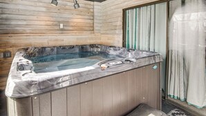 Ein Whirlpool in einem Holzraum mit einer Sitzbank, einem Fenster mit Vorhängen und einer Tür.