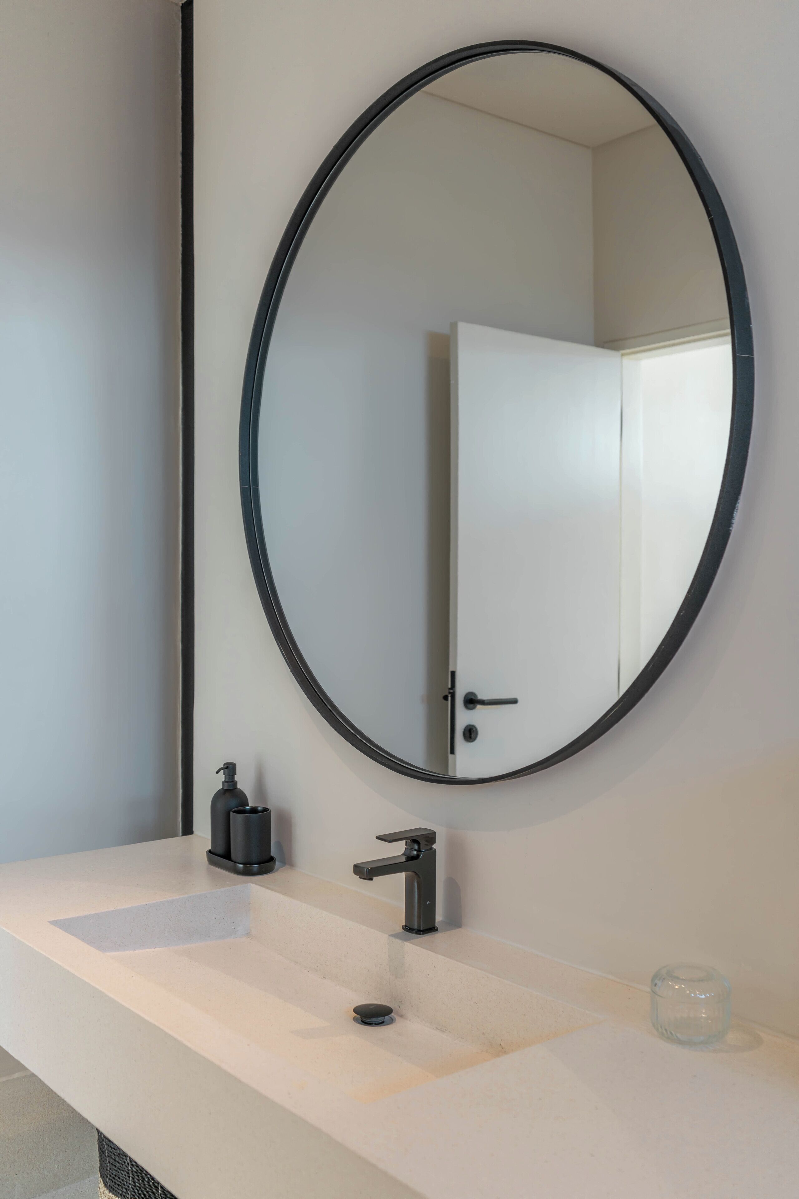 A bathroom with a white sink, a black faucet, a round mirror, and a white door.
