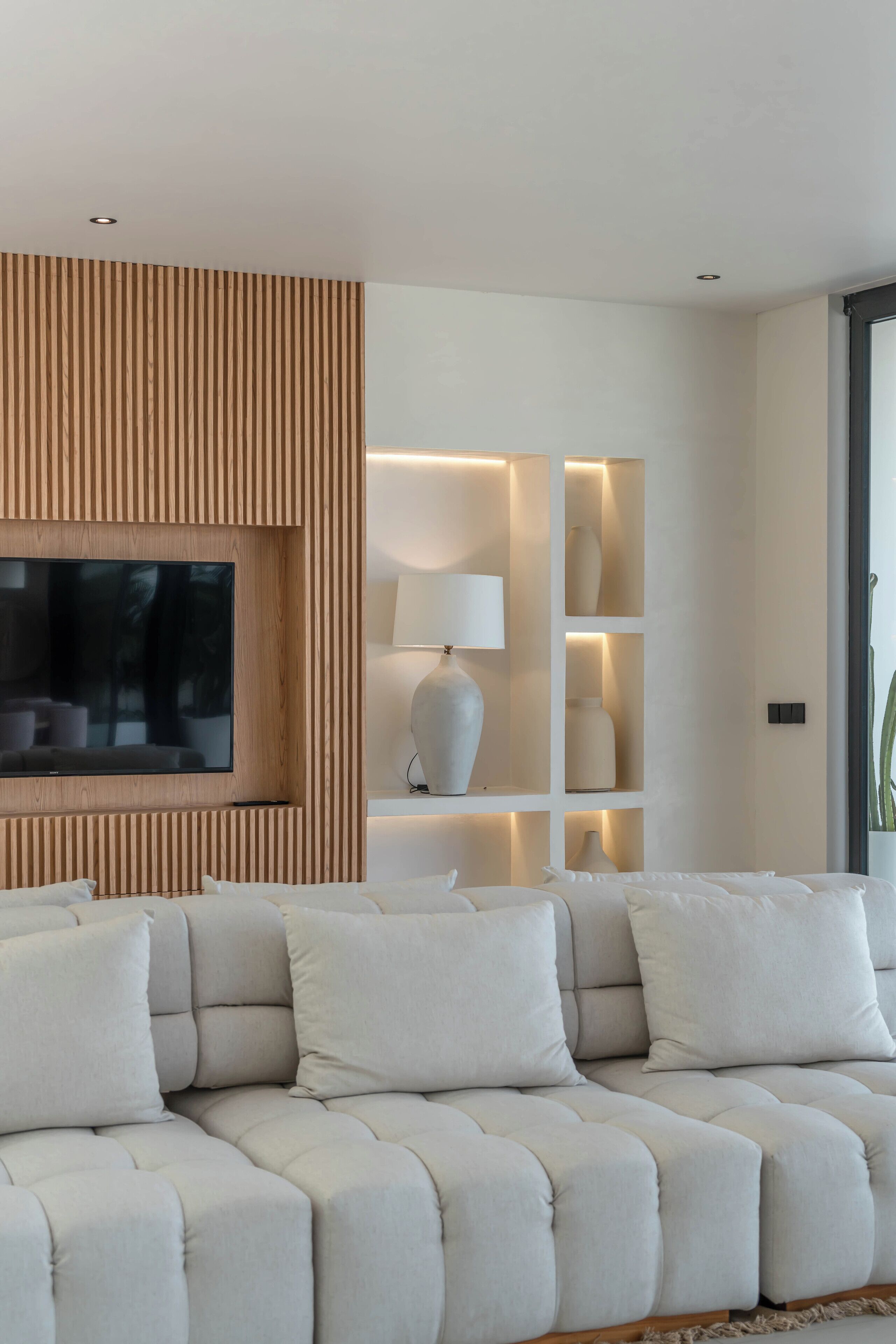 A modern living room with a sectional sofa, a flat-screen TV, and built-in shelving with decorative items.