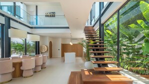 A modern interior with a central staircase, a seating area with cushioned chairs, and a large window overlooking greenery. - Villa Maverick (Canggu)