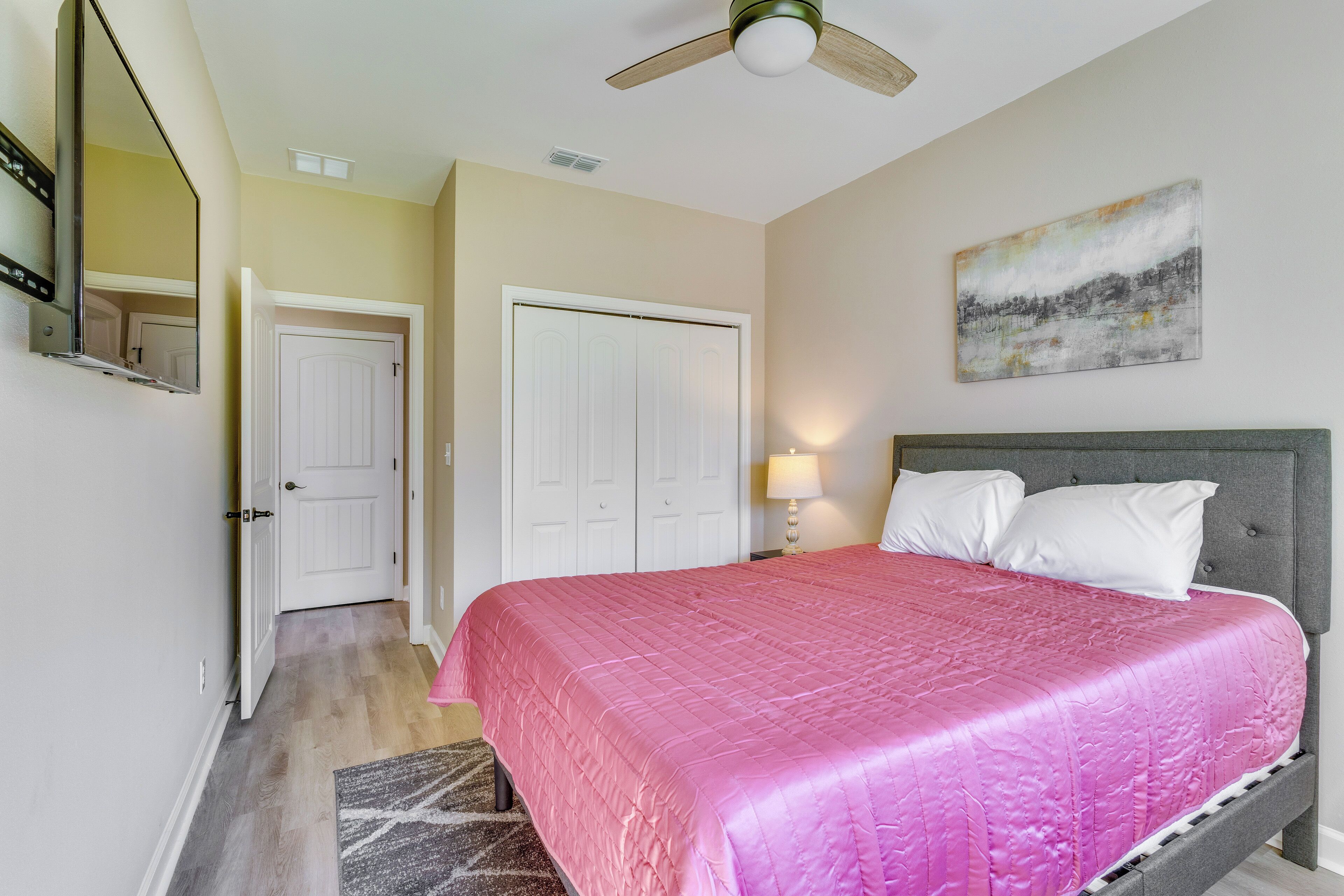 A bedroom with a bed, a ceiling fan, a door, and a painting on the wall.