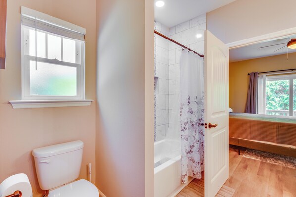 Een badkamer met toilet, douche met bloemen gordijn en bad.