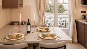 A dining area with a table set for four, two candles, a bottle of wine, and a view of the city through large windows.