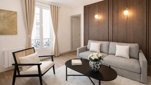A modern living room with a sofa, a coffee table, a chair, a window with curtains, and a wall-mounted light fixture.