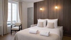 A hotel room with a bed, a chair, a window with curtains, and a door.