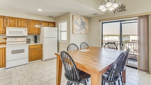 A kitchen with wooden cabinets, a white stove, and a refrigerator. There is a dining table with chairs and a view of the outside through a window.
