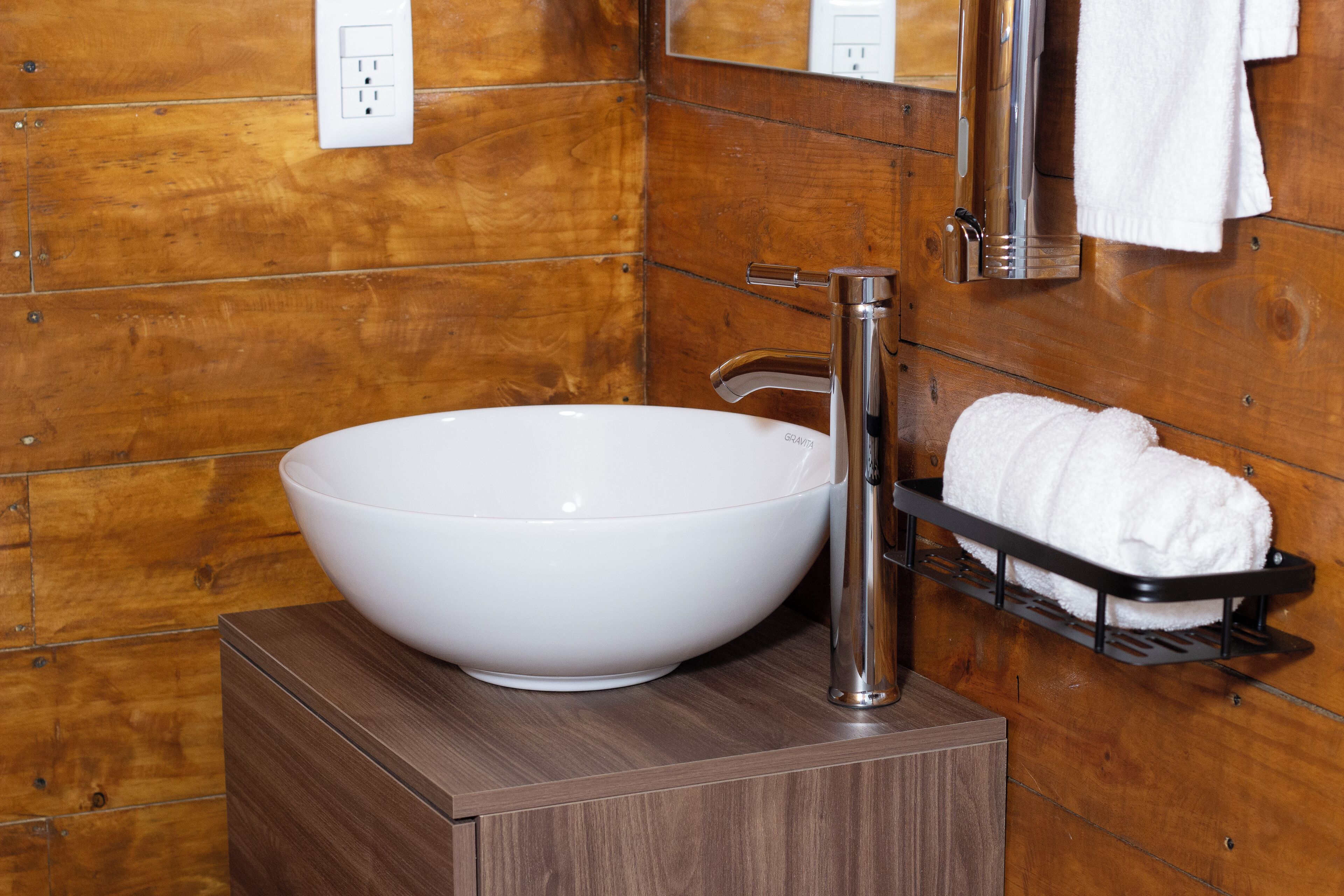Un baño con un lavamanos blanco de diseño, un grifo cromado, un perchero y paneles de madera.