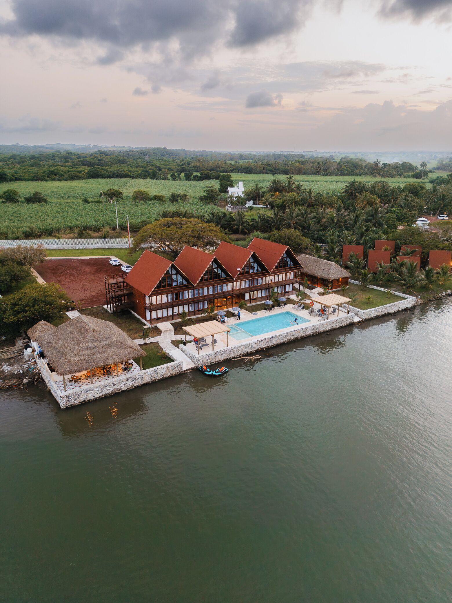 A large building with multiple rooms, a swimming pool, and a dock extending into a body of water.