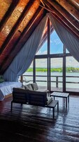 Habitación en el ático con cama, sofá y mesa, con vistas a un cuerpo de agua y vegetación.