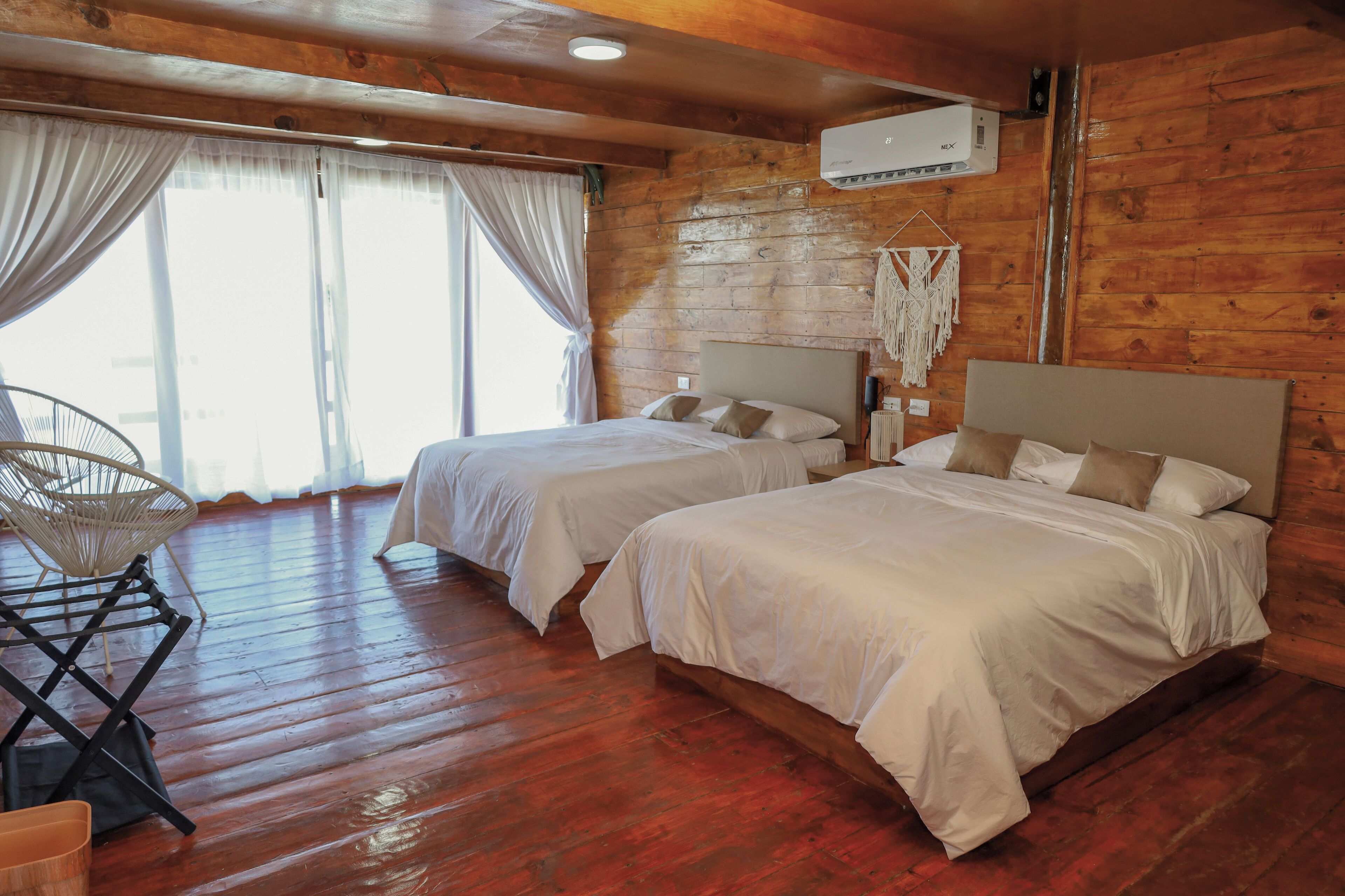 Una habitación con dos camas, pisos de madera, ventilador de techo y una ventana con cortinas.