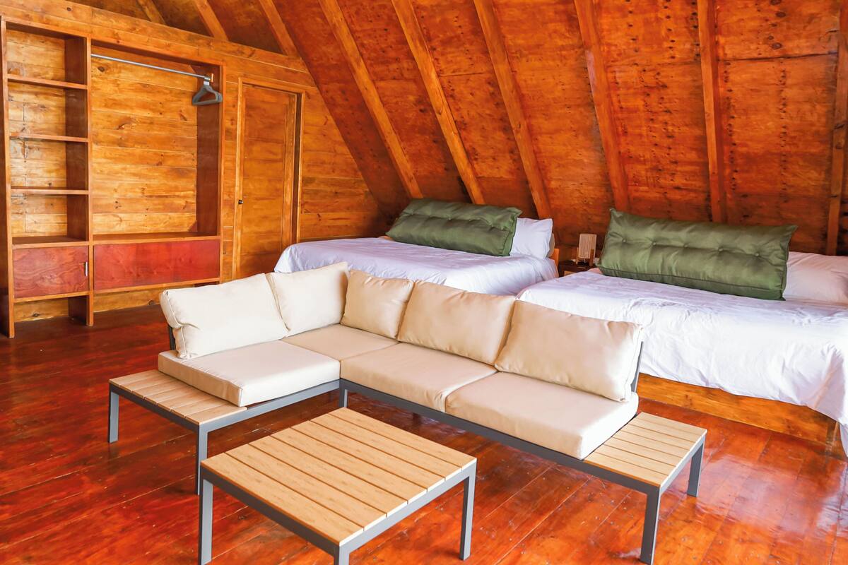 Ein gemütliches Schlafzimmer im Dachgeschoss mit Holzwänden, einer Couch, zwei Betten und Holzdielen.