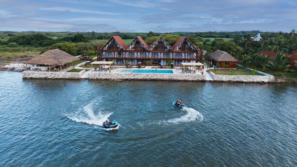 A large resort with a swimming pool, a thatched-roof structure, and a large building with multiple windows.