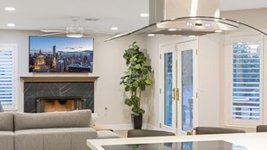 A modern living room with a fireplace, a large cityscape painting, a ceiling fan, and a dining area with a glass table. - The Blue Lagoon: Where Space, Style and Comfort collide! (Las Vegas)