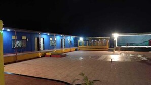 Ein Hotelinnenhof bei Nacht mit einem blauen Gebäude, einer überdachten Sitzgelegenheit und einem Brunnen.