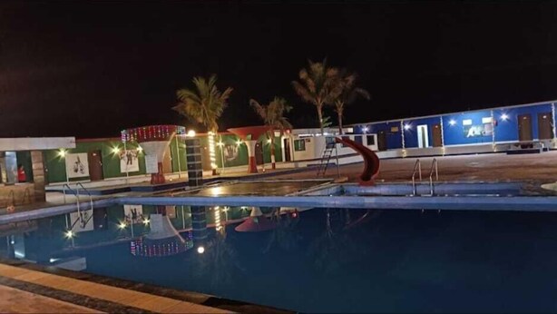 Ein Swimmingpool mit Wasserrutsche, Palmen und einem Gebäude mit blauer Fassade.