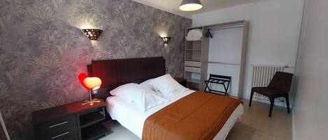 A bedroom with a bed, nightstands, a red lamp, a wardrobe, and a chair.