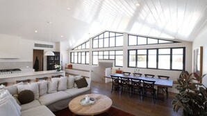 A spacious living area with a high ceiling, large windows, a dining table, and a sofa. - Luxurious Beach House with Breath-taking Views (Ocean Grove)