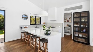 A modern kitchen with a central island, bar stools, and a black cabinet with glass doors. - Luxurious Beach House with Breath-taking Views (Ocean Grove)