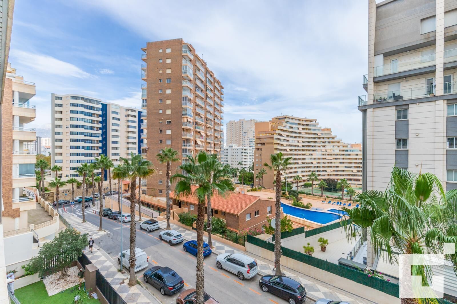 A high-rise residential building with multiple balconies, a swimming pool, and palm trees.
