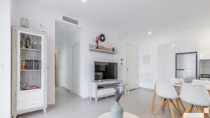 A modern living room with a TV, white furniture, and a dining area with a table and chairs. - Calpe Beach II 3C - Grupo Turis - Calpe, Costa Blanca (Calpe)