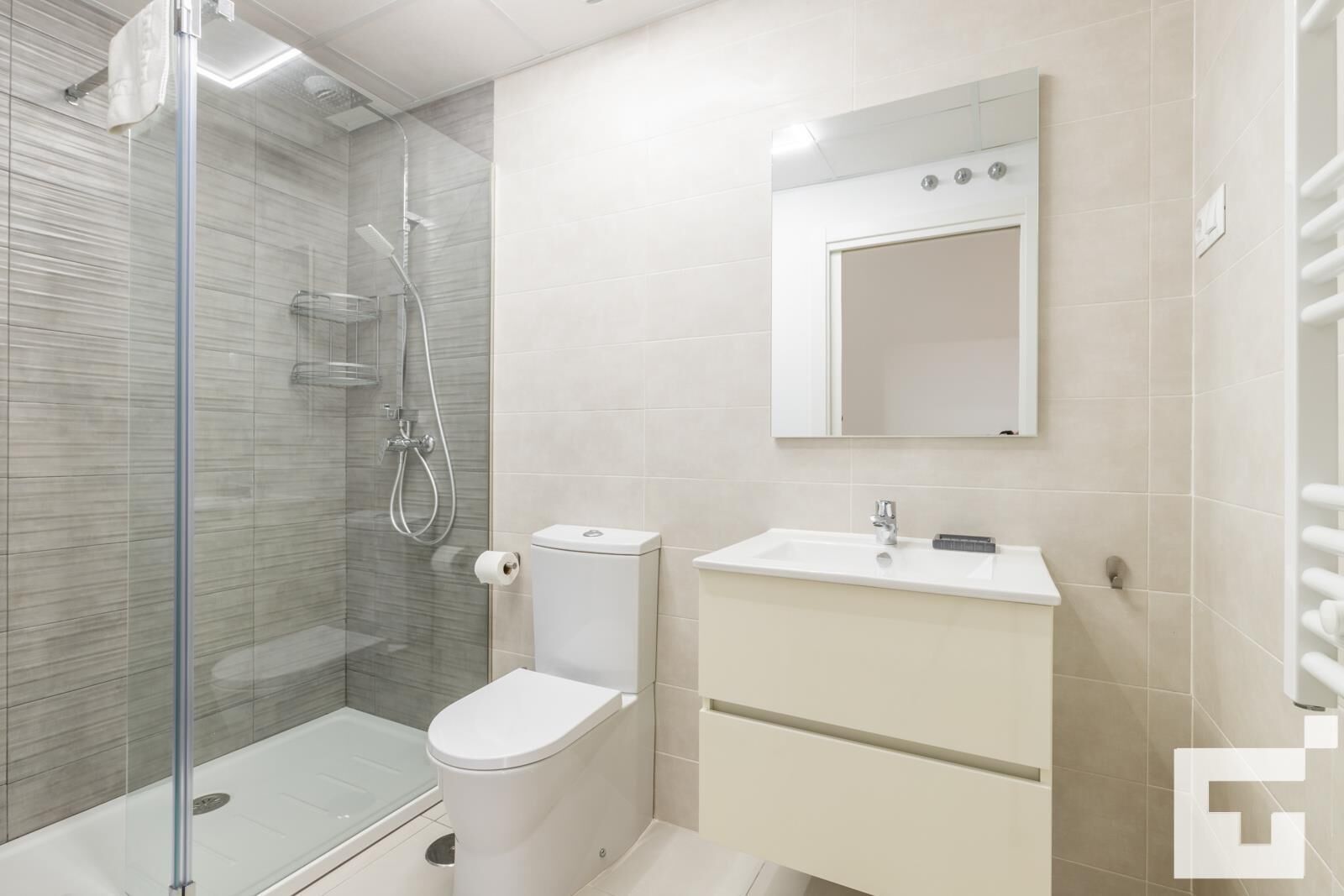 Une salle de bain moderne avec une douche à parois de verre, des toilettes et un lavabo surmonté d’un miroir.