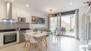 A modern kitchen with a dining area, a sofa, and a balcony with a view of buildings. - Calpe Beach II 3C - Grupo Turis - Calpe, Costa Blanca (Calpe)