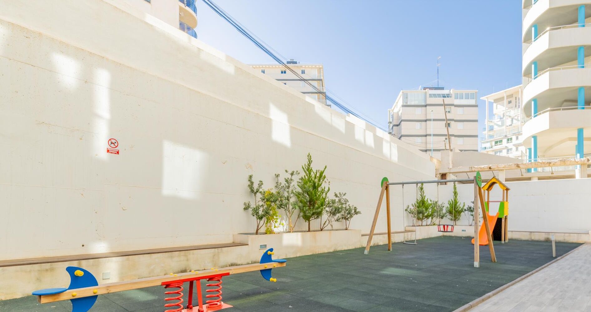 A rooftop playground with swings and a slide, surrounded by buildings.
