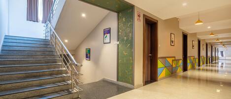 A hotel lobby with a staircase, a reception desk, and a hallway leading to other rooms.
