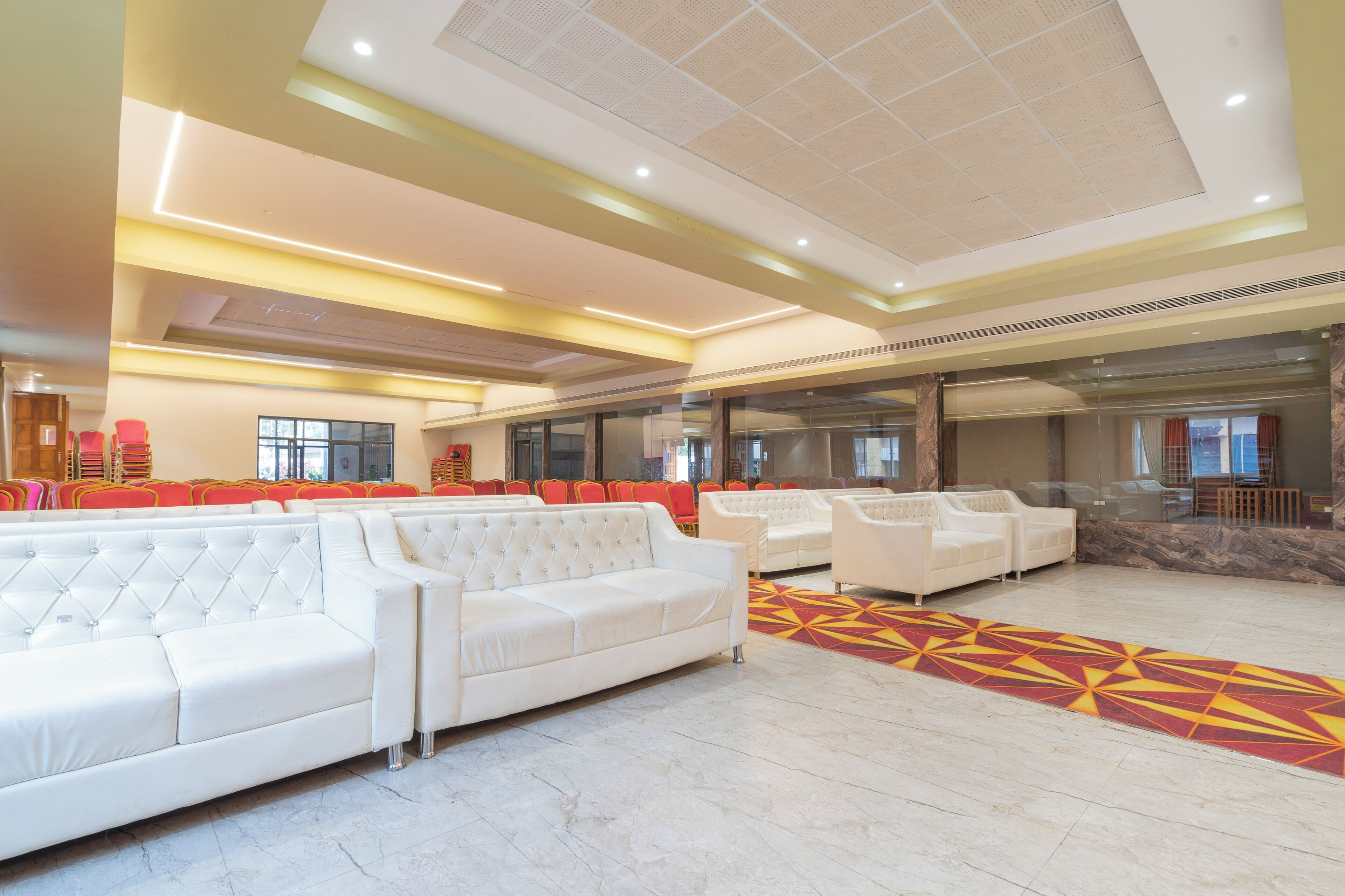 A spacious lobby with a white sofa, red chairs, and a patterned carpet.