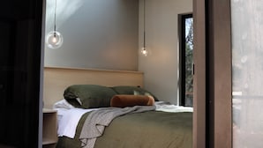 Een moderne slaapkamer met een houten hoofdbord, een bed met groen en bruin beddengoed, en twee hanglampen.