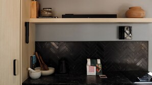 Een moderne keuken met een zwart ruitpatroon achterwand, een houten plank met een vaas en een boek, en een koffiezetapparaat op het aanrecht.