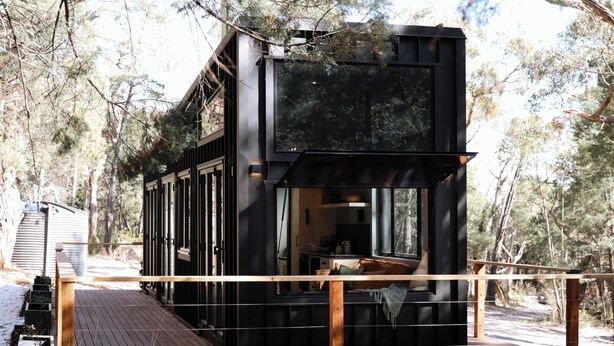 Een moderne cabin met een terras, grote ramen en uitzicht op het omliggende bos.