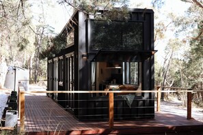 Une cabane moderne dotée d’une terrasse, de grandes fenêtres et offrant une vue sur la forêt environnante.